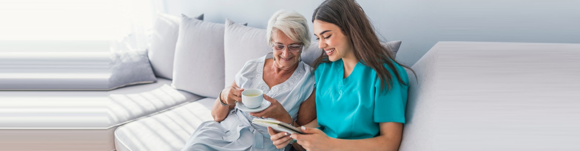 caregiver and senior woman holding a cup of tea smiling