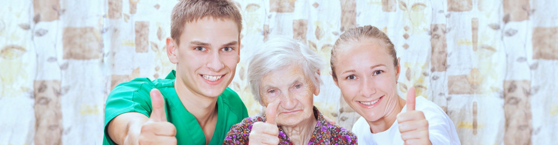 male and female caregiver with senior woman thumbs up and smiling